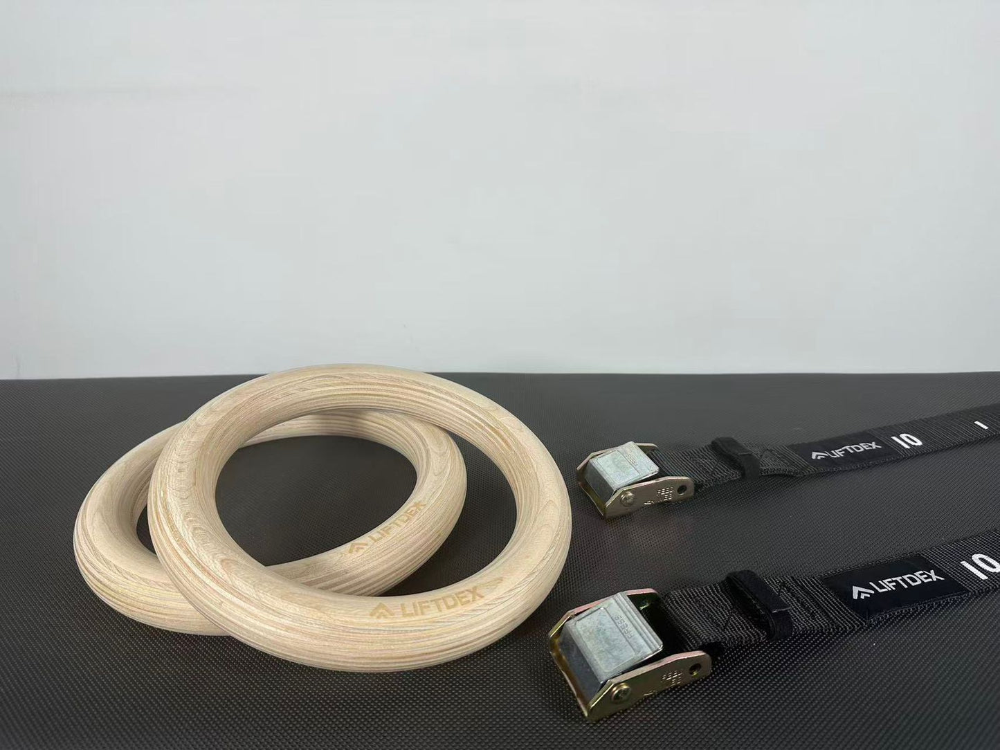 Wooden rings and black straps with visible branding on a dark surface.