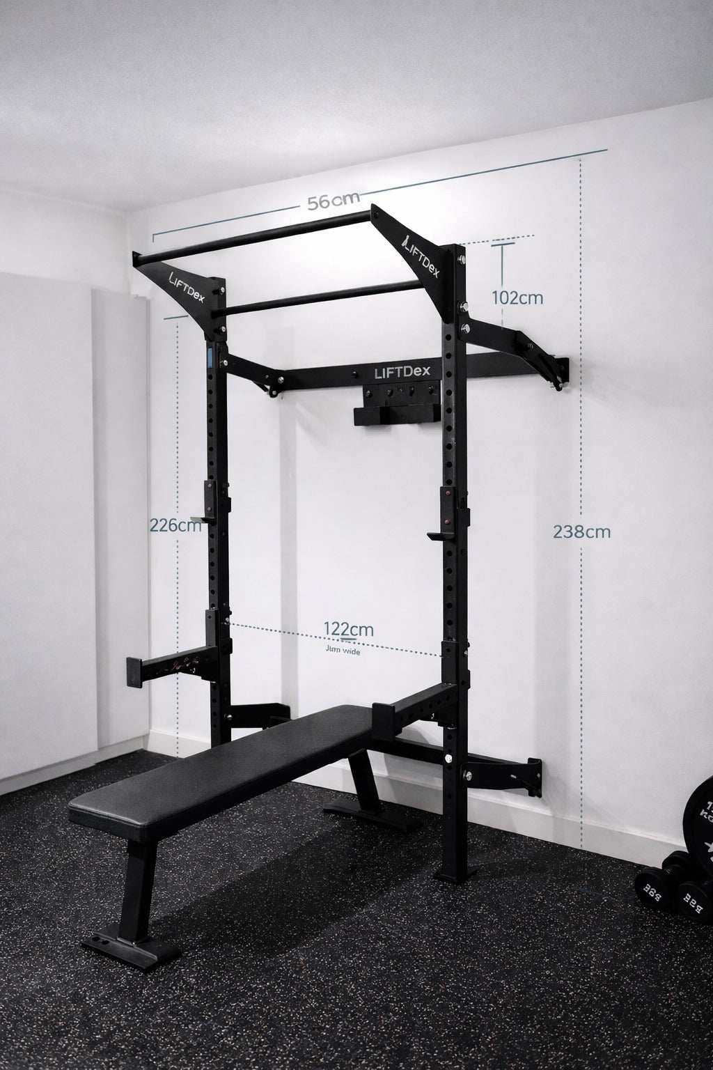 Gym power rack with bench and measurement markings on a white wall.