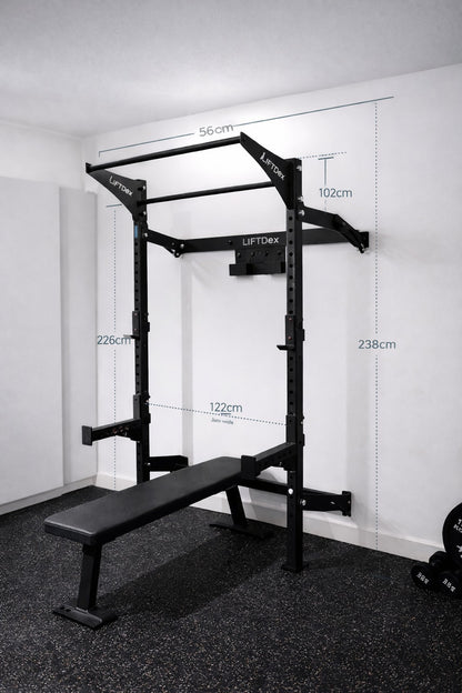 Gym power rack with bench and measurement markings on a white wall.